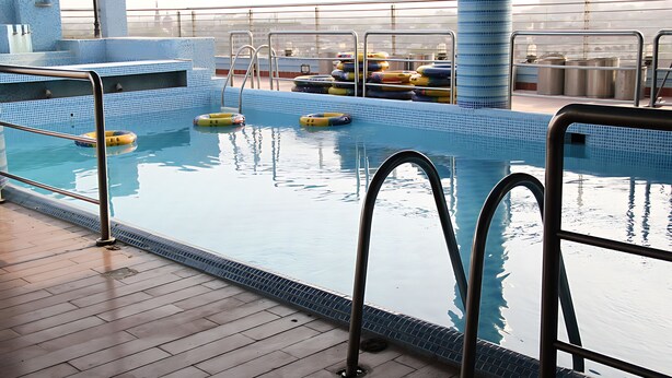 Zona de piscina con agua cristalina, barandillas metálicas y anillos flotantes.