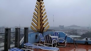 Terraza en la azotea con sillones de sala reclinables a rayas azules y blancas, una estructura decorativa amarilla y vistas de la ciudad al fondo.