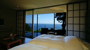 A bedroom with a large bed, a small table with a vase, and a view of the ocean through floor-to-ceiling windows. - Gensen to Hanare no Oyado Tsuki (Ito)