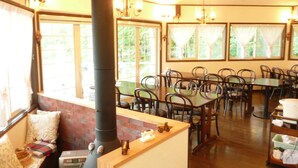 Um restaurante acolhedor com mesas e cadeiras de madeira, uma lareira grande e amplas janelas com cortinas.