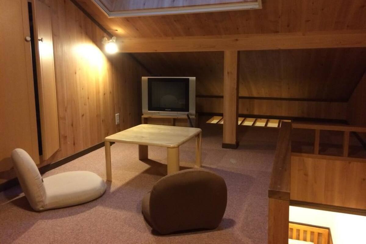 Ein gemütliches Dachzimmer mit Fernseher, einem gepolsterten Sessel und einem kleinen Tisch.