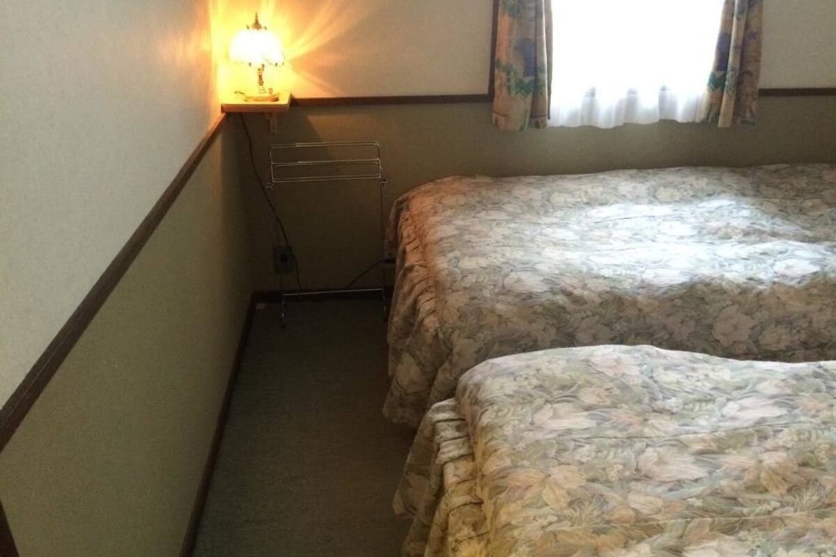 Ein Zimmer mit zwei Betten, einem Nachttisch mit Lampe und einem Fenster mit Vorhängen.