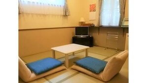 Quarto com sofá, mesinha, televisão e janela com cortinas.