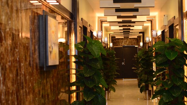 Een hotelgang met een marmeren wand, kamerplanten en moderne verlichtingsarmaturen.