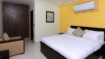 A hotel room with a bed, a wardrobe, a bedside table, and an air conditioning unit on the wall.
