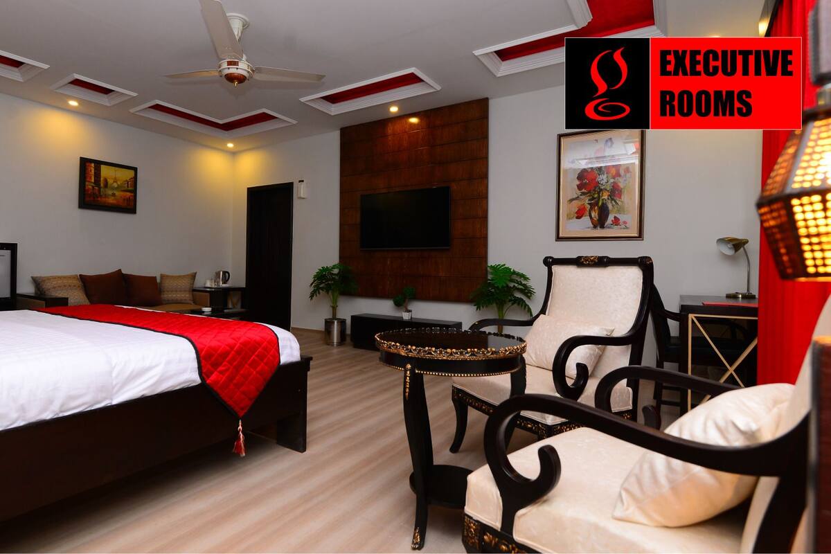 A hotel room with a large bed, a desk, a chair, a TV, and a ceiling fan.