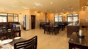 A spacious restaurant with multiple dining tables and chairs, a kitchen area, and large windows allowing natural light. - Charekh Food & Forest Resort (Lansdowne)