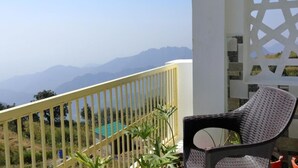 A balcony with a yellow railing, a wicker chair, and a view of distant mountains. - Charekh Food & Forest Resort (Lansdowne)