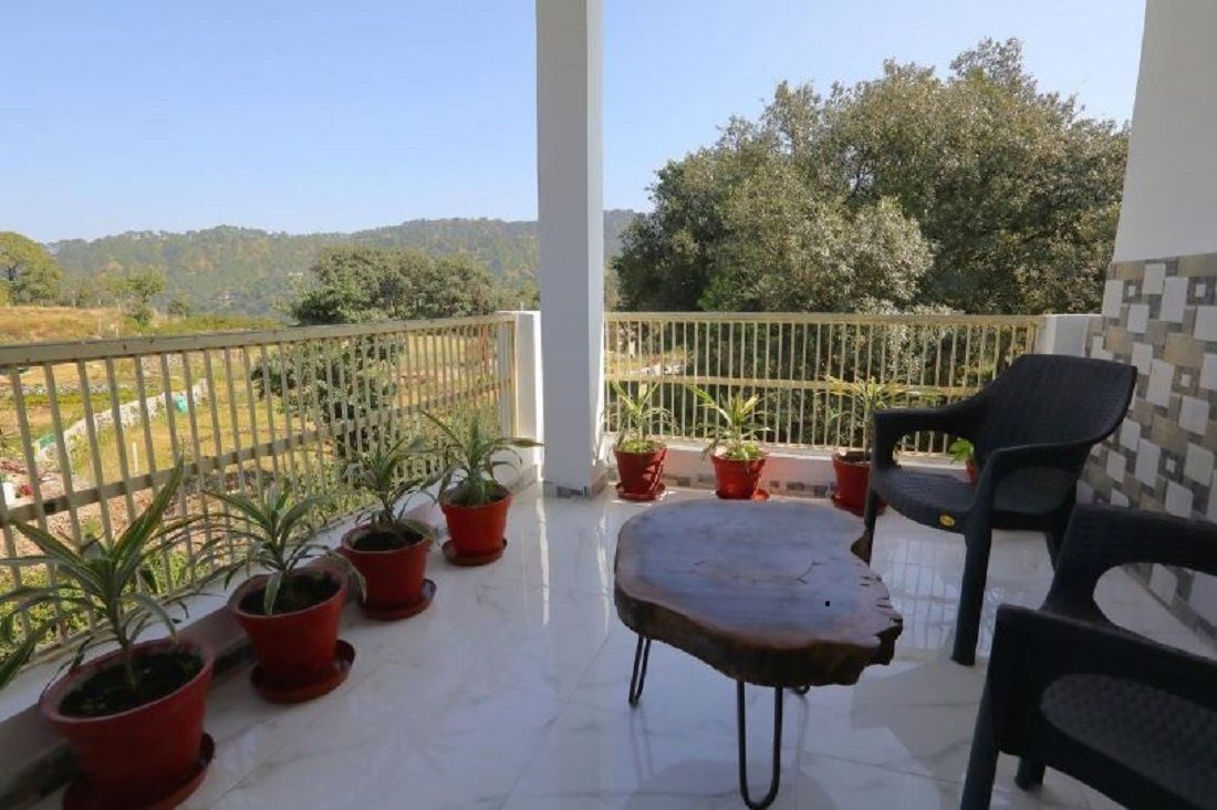 Un balcón con vistas a un paisaje montañoso, plantas en macetas y una mesa con sillas.