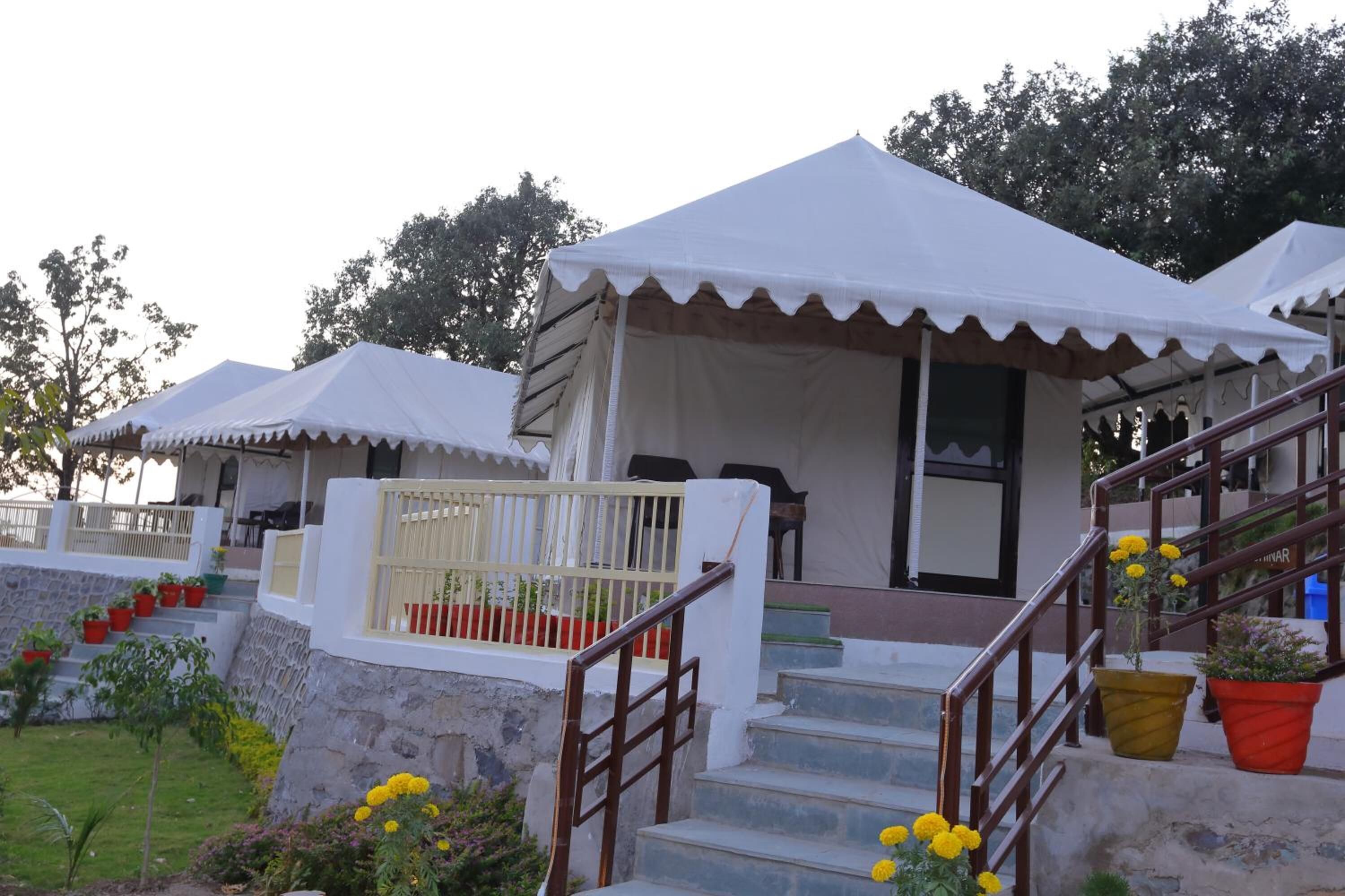 A series of white tents with steps leading up to a covered entrance, surrounded by potted plants and a stone wall.