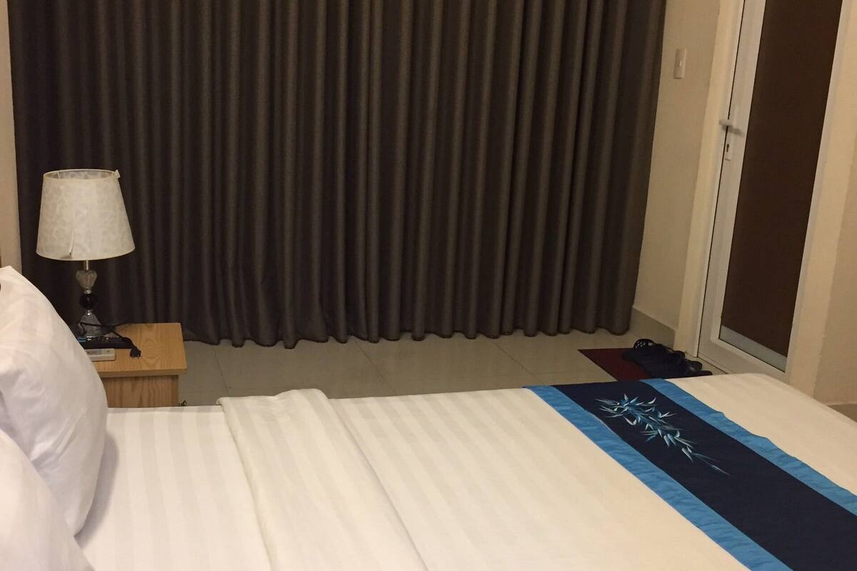 A hotel room with a bed, a nightstand with a lamp, and a door.