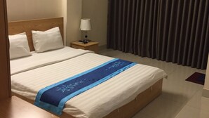 Una camera d'albergo con un letto grande, un comodino, una lampada, un quadro appeso al muro e una finestra con tende.
