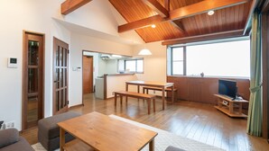 Un amplio salón con suelo de madera, una mesa de comedor, bancos, un sofá y un televisor.