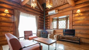 Ein rustikales Blockhaus-Interieur mit einer Couch, einem Tisch, einem Fernseher und einem Kamin aus Stein.