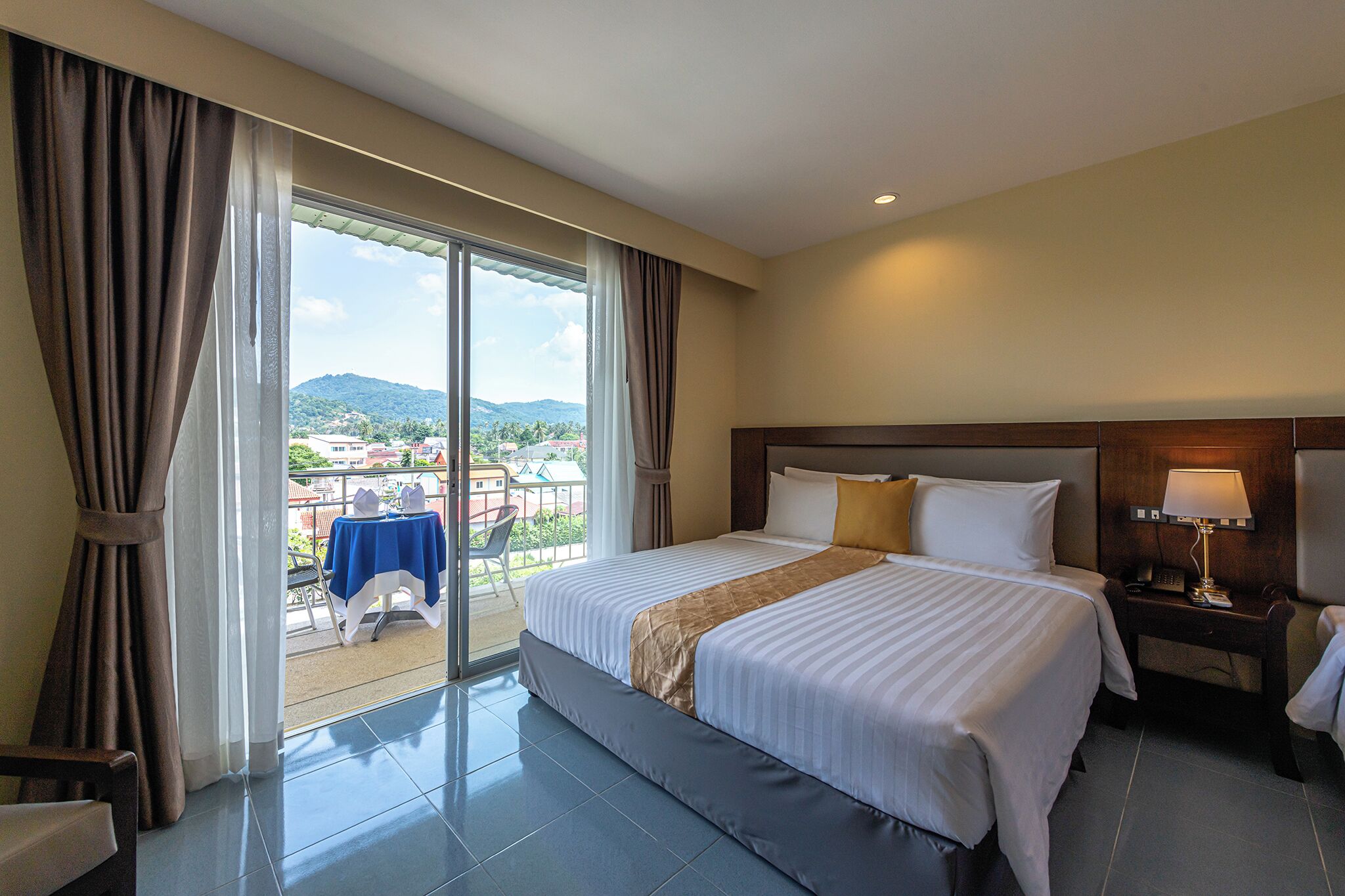 A hotel room with a large bed, a nightstand with a lamp, and a view of the outdoors through a sliding door.