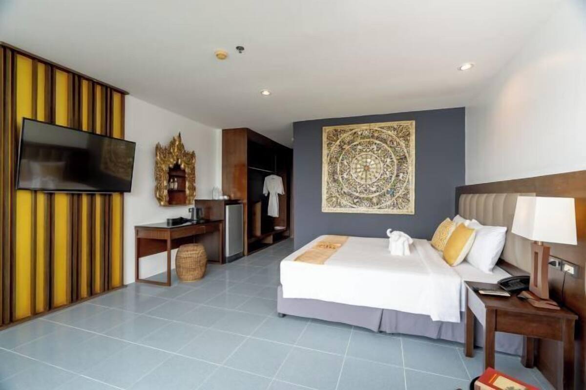 A hotel room with a bed, bedside table, TV, wardrobe, and a decorative wall piece.