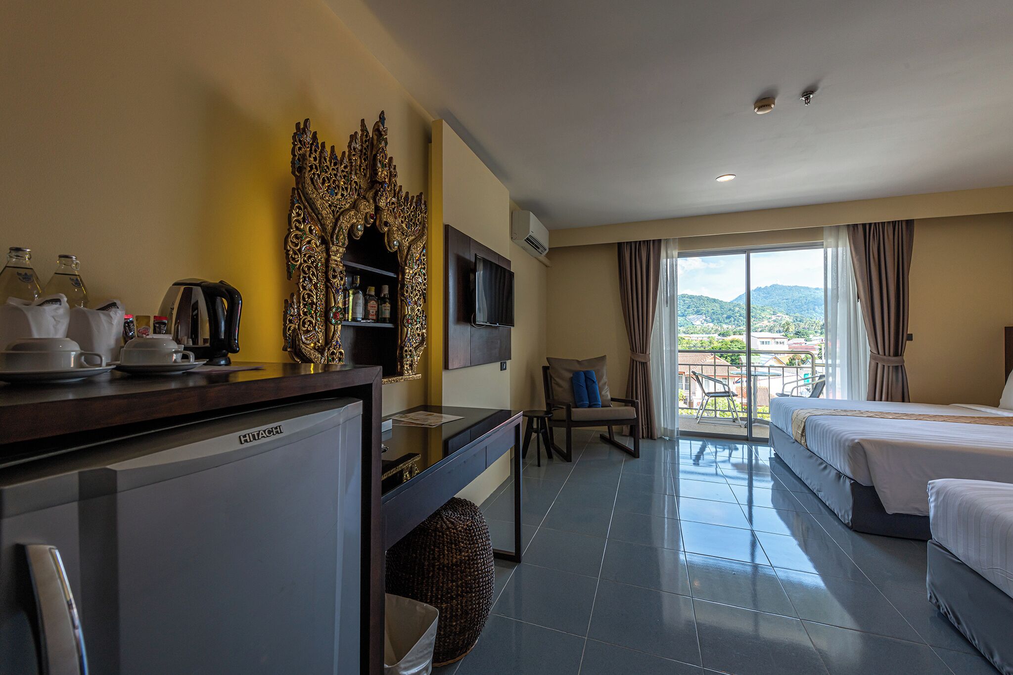 A hotel room with a kitchenette, a TV, a sofa, two beds, and a balcony with a view.