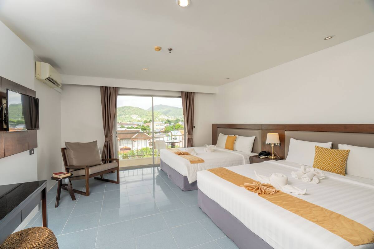 A hotel room with two beds, a TV, a desk, and a view of the outdoors.