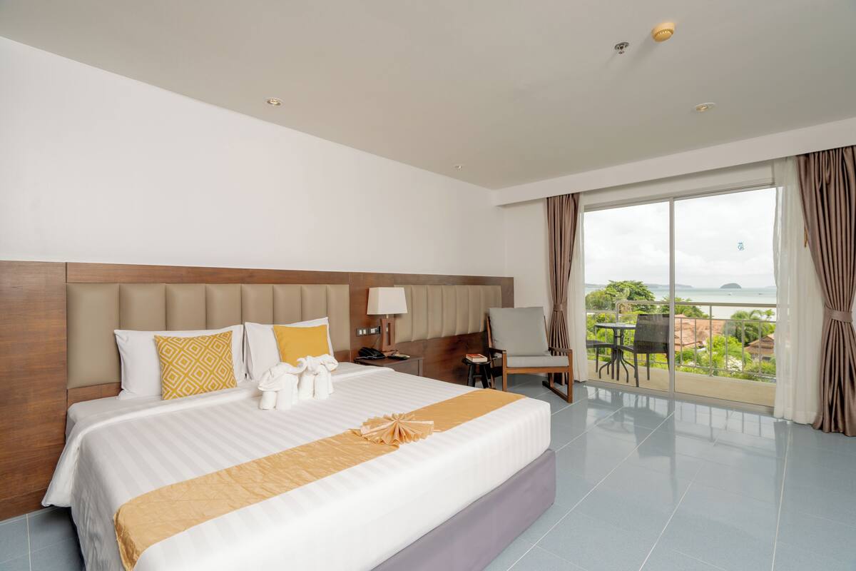 A hotel room with a large bed, a desk, a chair, and a balcony with a view.
