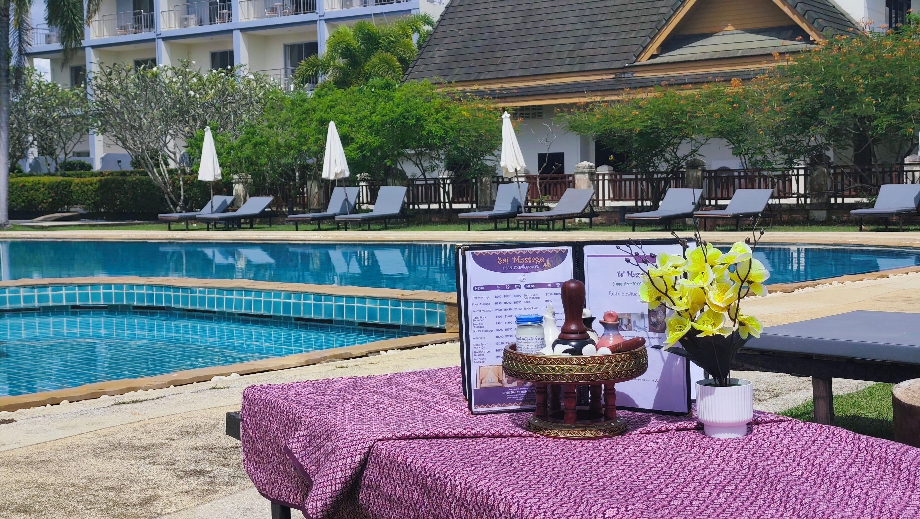 Zona de piscina con sillas de descanso, una mesa con menú y un jarrón decorativo.