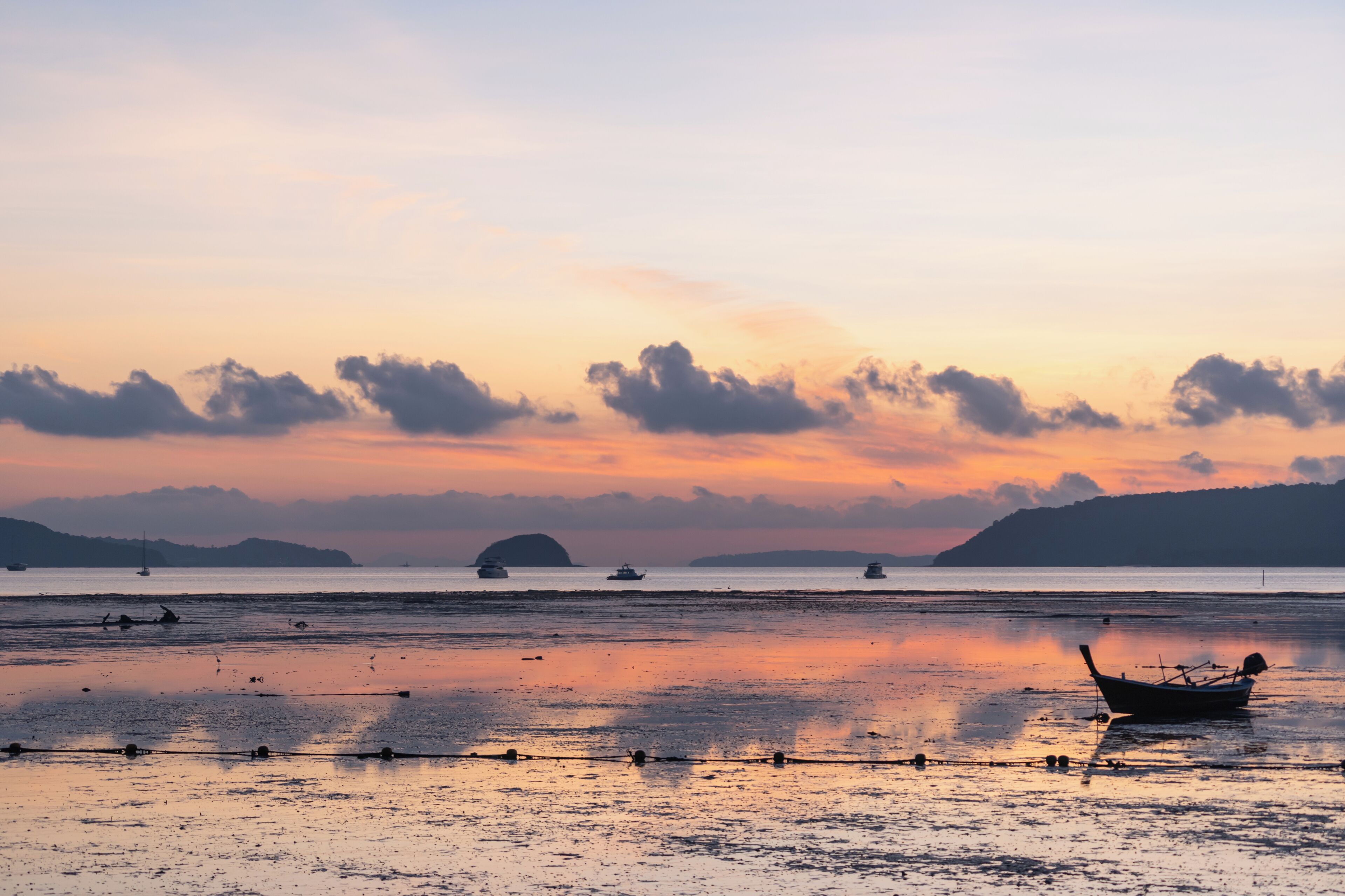 A boat on a calm beach with distant boats and a sunset.