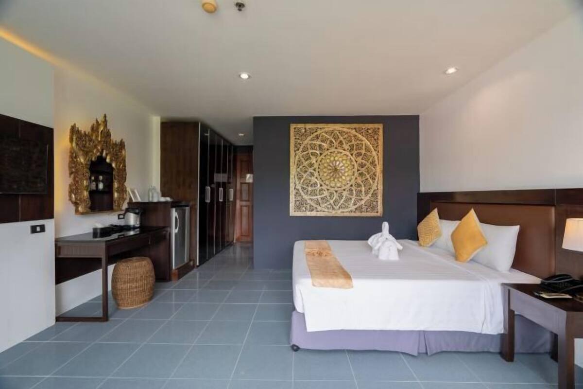 A hotel room with a bed, a desk, a kitchenette, and a decorative wall piece.