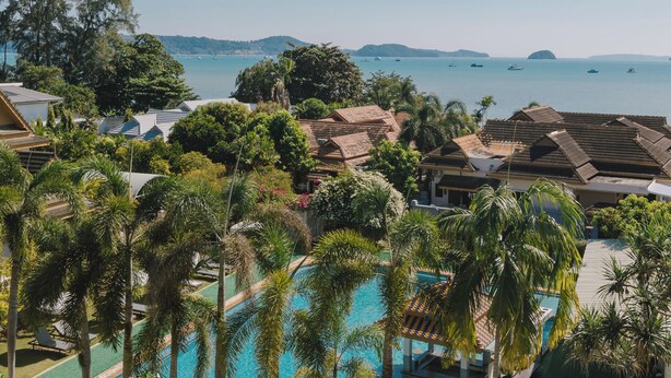Un resort con piscina rodeada de palmeras y vistas al mar.