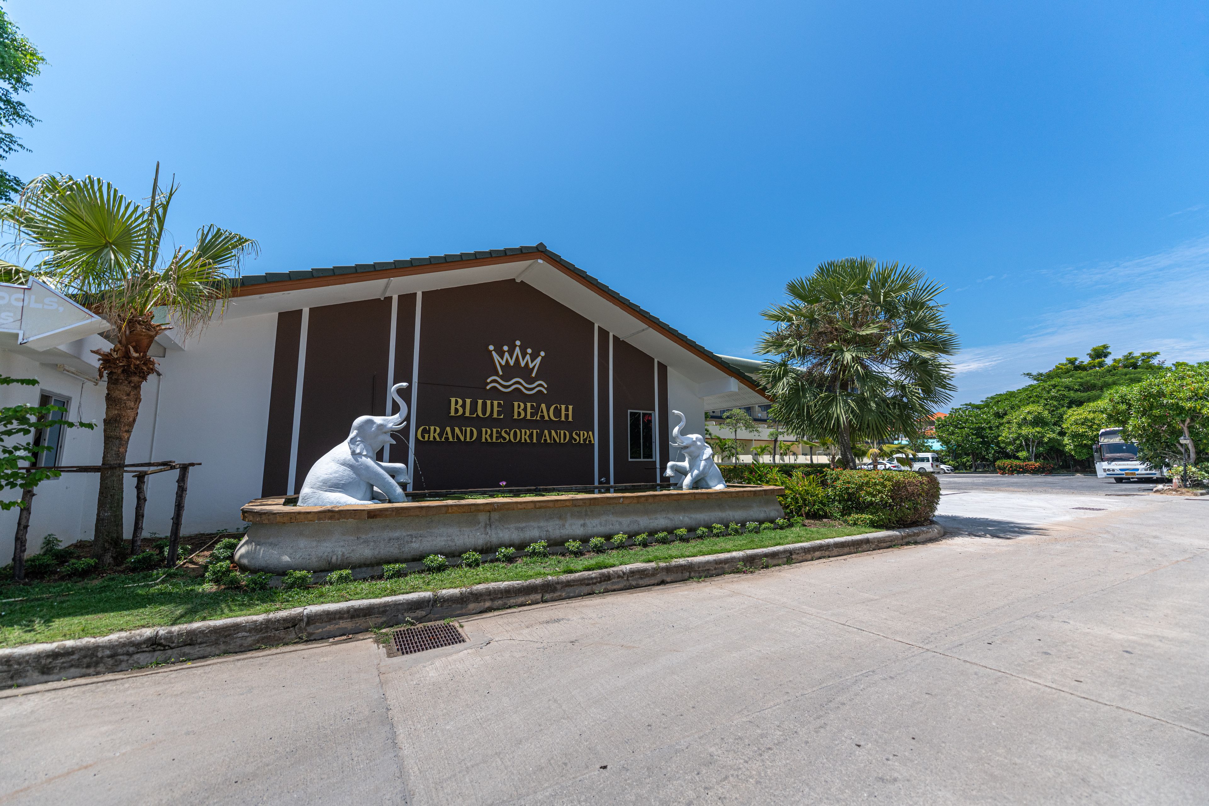 A building with a sign reading "Blue Beach Grand Resort and Spa" and two white elephant statues in front.