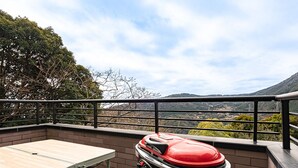 Un patio en la azotea con una parrilla, una mesa y vistas a un paisaje montañoso.