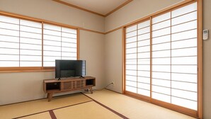 Una habitación tradicional japonesa con suelo de tatami, un televisor sobre un soporte de madera y puertas correderas shoji.