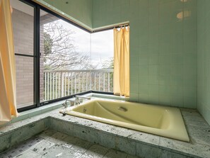 A bathroom with a bathtub, a window with a view, and a balcony with a railing.