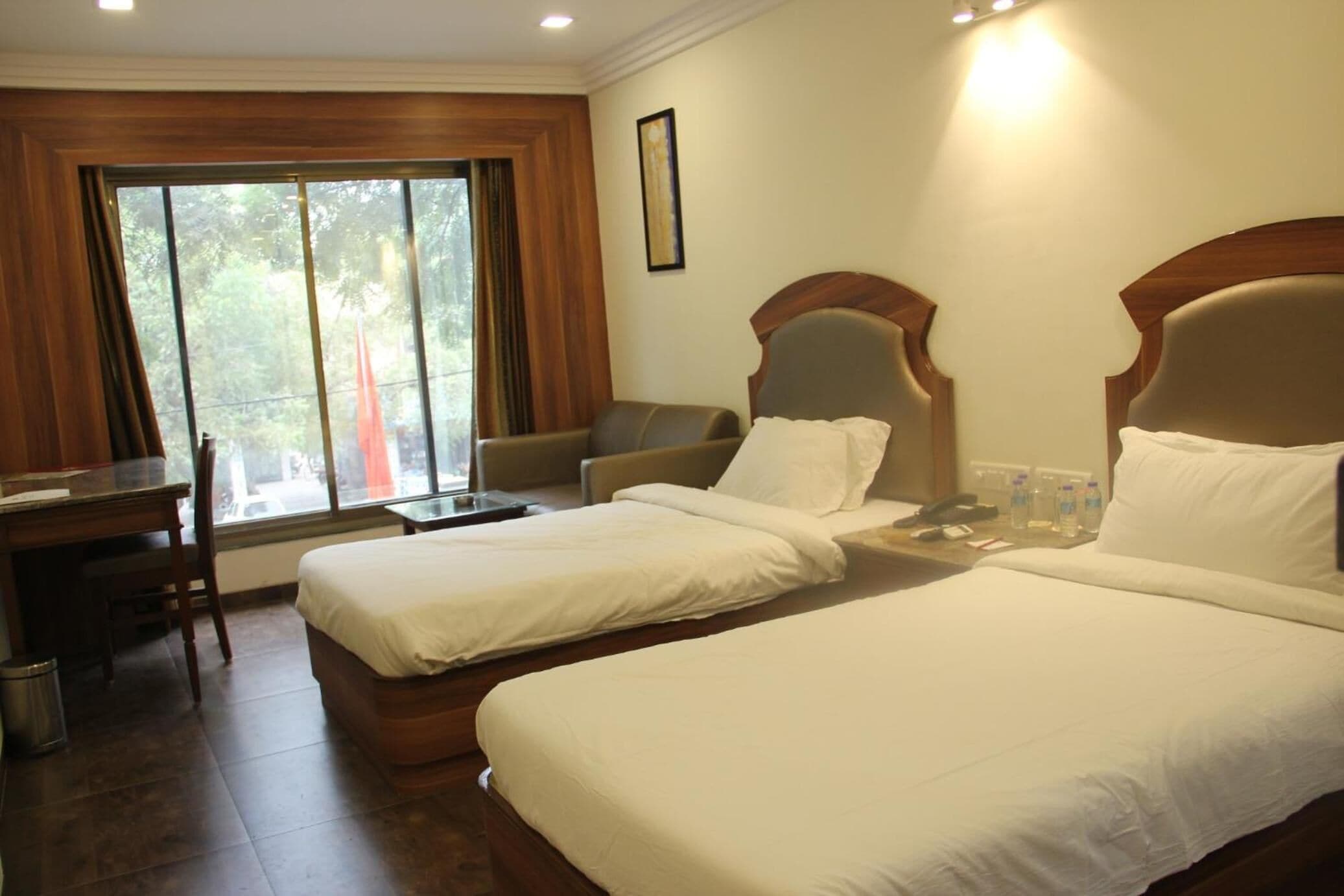 A hotel room with two beds, a desk, a chair, and a window with curtains.