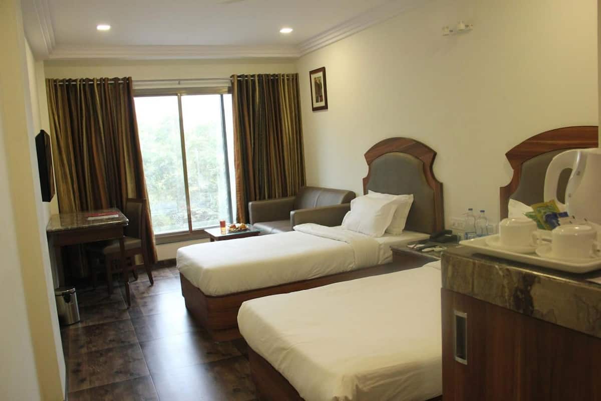 A hotel room with two beds, a desk, a chair, a coffee maker, and a window with curtains.