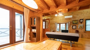 A wooden cabin interior with a wooden table, a bench, a sofa, and a large window offering a view. - Angel Forest Izu Kogen (Ito)
