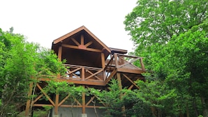 A wooden cabin with a balcony, surrounded by dense trees. - Angel Forest Izu Kogen (Ito)