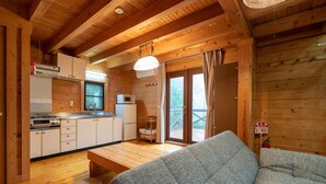 A cozy cabin interior with a wooden floor, a sofa, a dining table, and a kitchen area including a microwave and cabinets. - Angel Forest Izu Kogen (Ito)