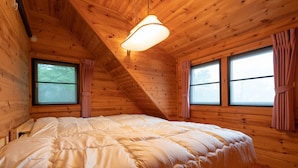 A wooden cabin bedroom with a large bed, two windows with curtains, and a sloped ceiling. - Angel Forest Izu Kogen (Ito)