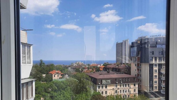 A view from a window overlooking a coastal cityscape with buildings, trees, and the sea. - Apartment Levanevskogo 7-53 (Odesa)