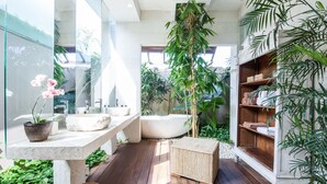 Une salle de bain moderne avec un plancher en bois, une baignoire, un grand miroir et diverses plantes.