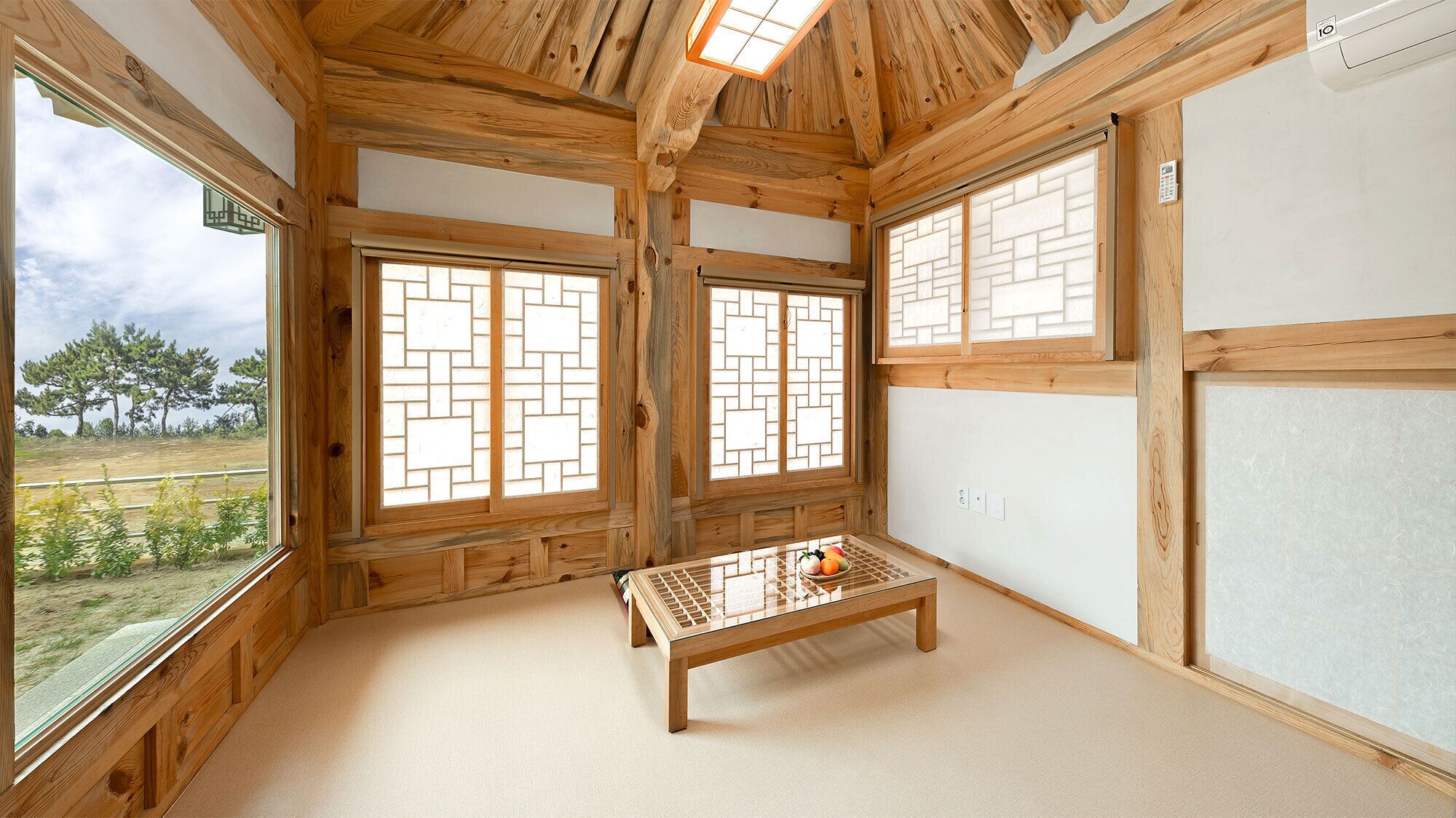 Quarto com vigas de madeira, piso de tatame, mesa baixa e janelas grandes com design de treliça tradicional.