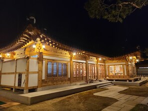 Una estructura de madera tradicional con tejado de baldosas y ventanas iluminadas, rodeada de un camino de piedra.