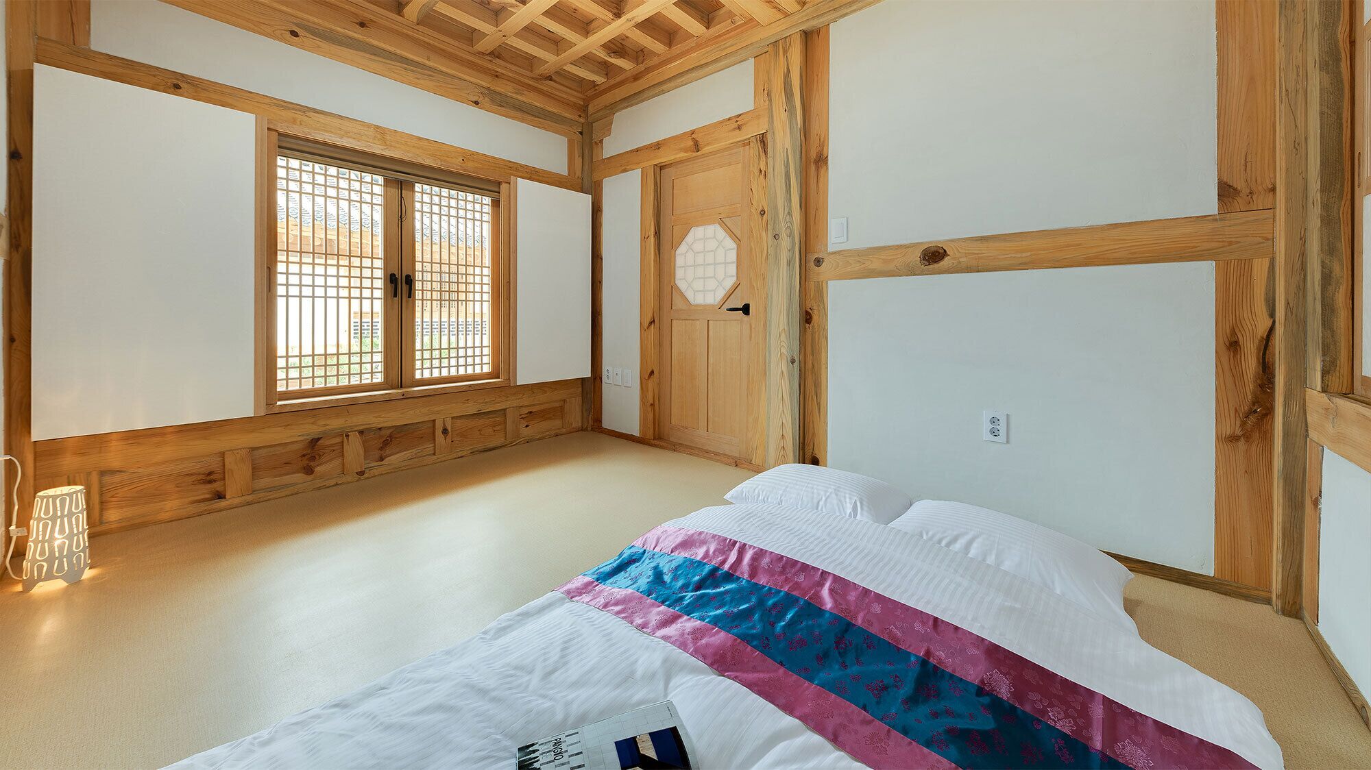 A traditional Japanese room with tatami flooring, a bed with a colorful bedspread, a shoji screen door, and a wooden ceiling.