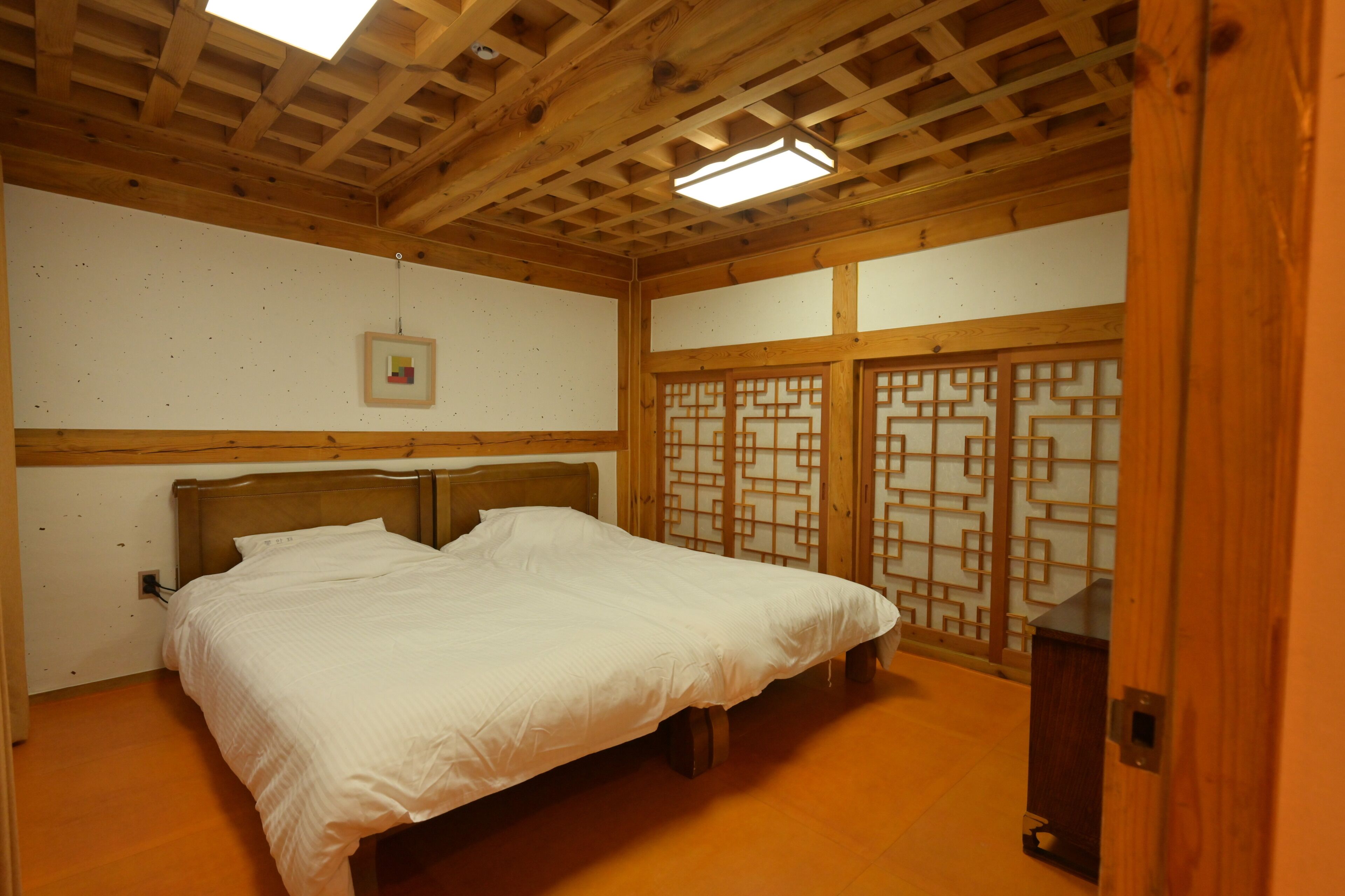 A bedroom with a wooden ceiling, a bed, a wall-mounted light, and a traditional door.