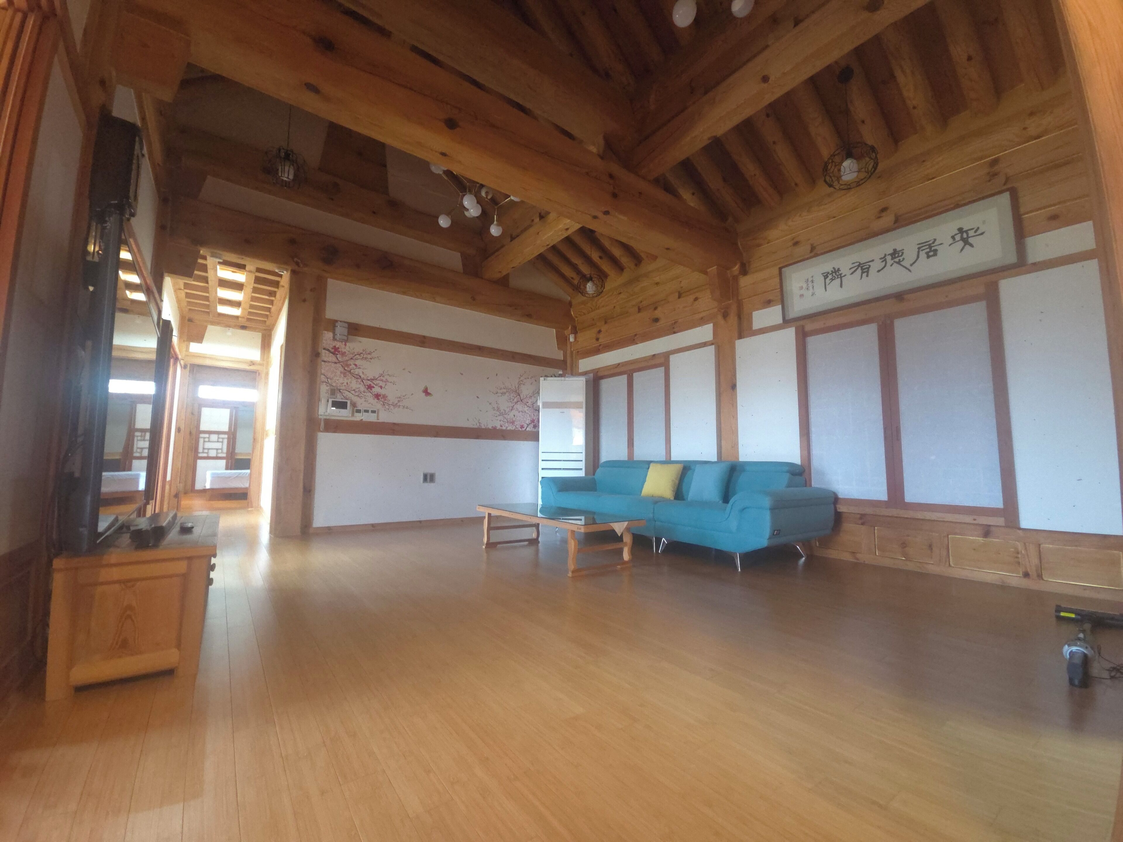 Una habitación amplia con techo de madera, un sofá azul, una mesita pequeña y una pared con un panel decorativo.