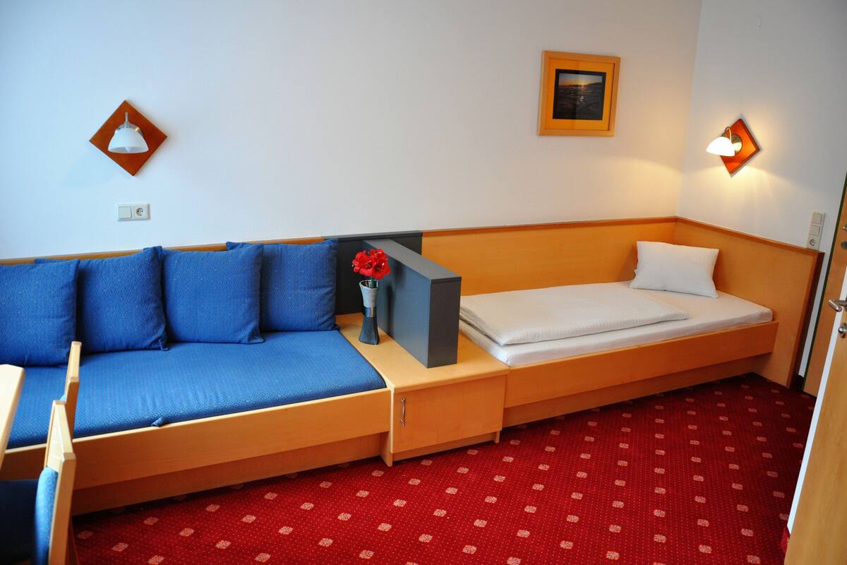 A compact room with a single bed, a small table, and a blue sofa.