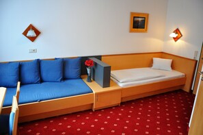 A compact room with a single bed, a small table, and a blue sofa. - Pension Posauner Dorfgastein (Dorfgastein)
