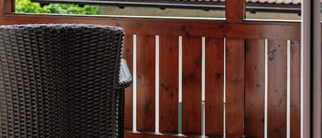 Una terraza de madera con una silla de mimbre, vista a una montaña y un edificio con tejado de baldosas.