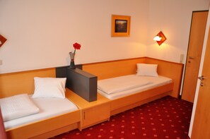 A hotel room with two single beds, a nightstand, a vase with a red flower, a framed picture on the wall, and a red patterned carpet. - Pension Posauner Dorfgastein (Dorfgastein)