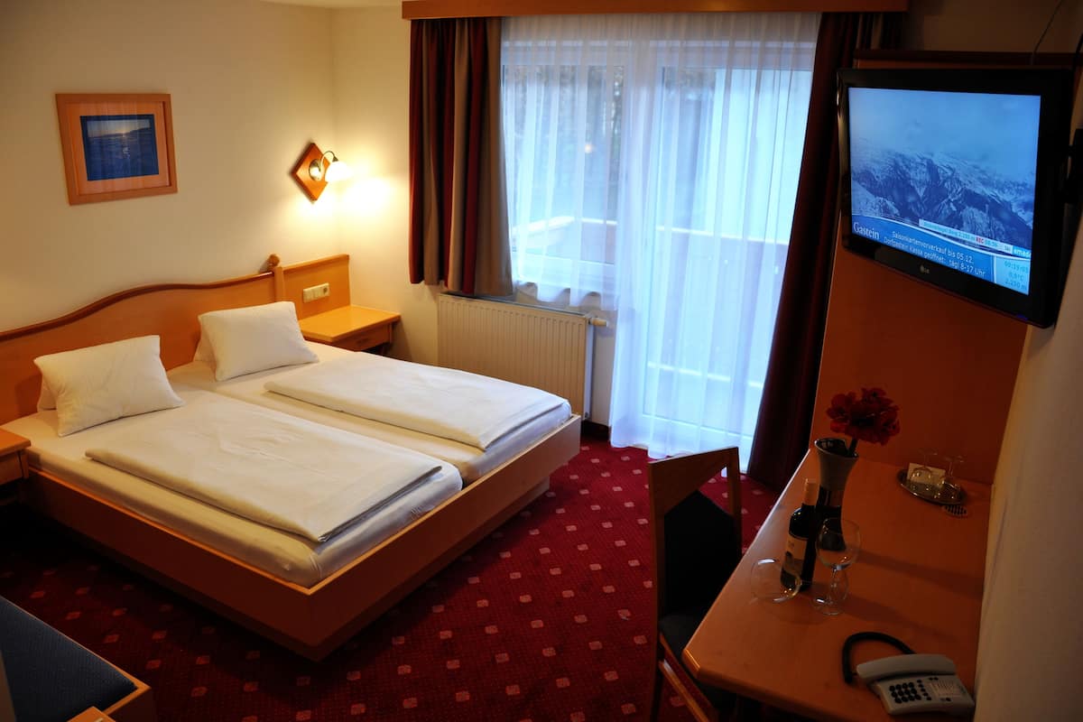 A hotel room with two beds, a desk with a telephone, a vase with flowers, and a TV displaying a snowy landscape.