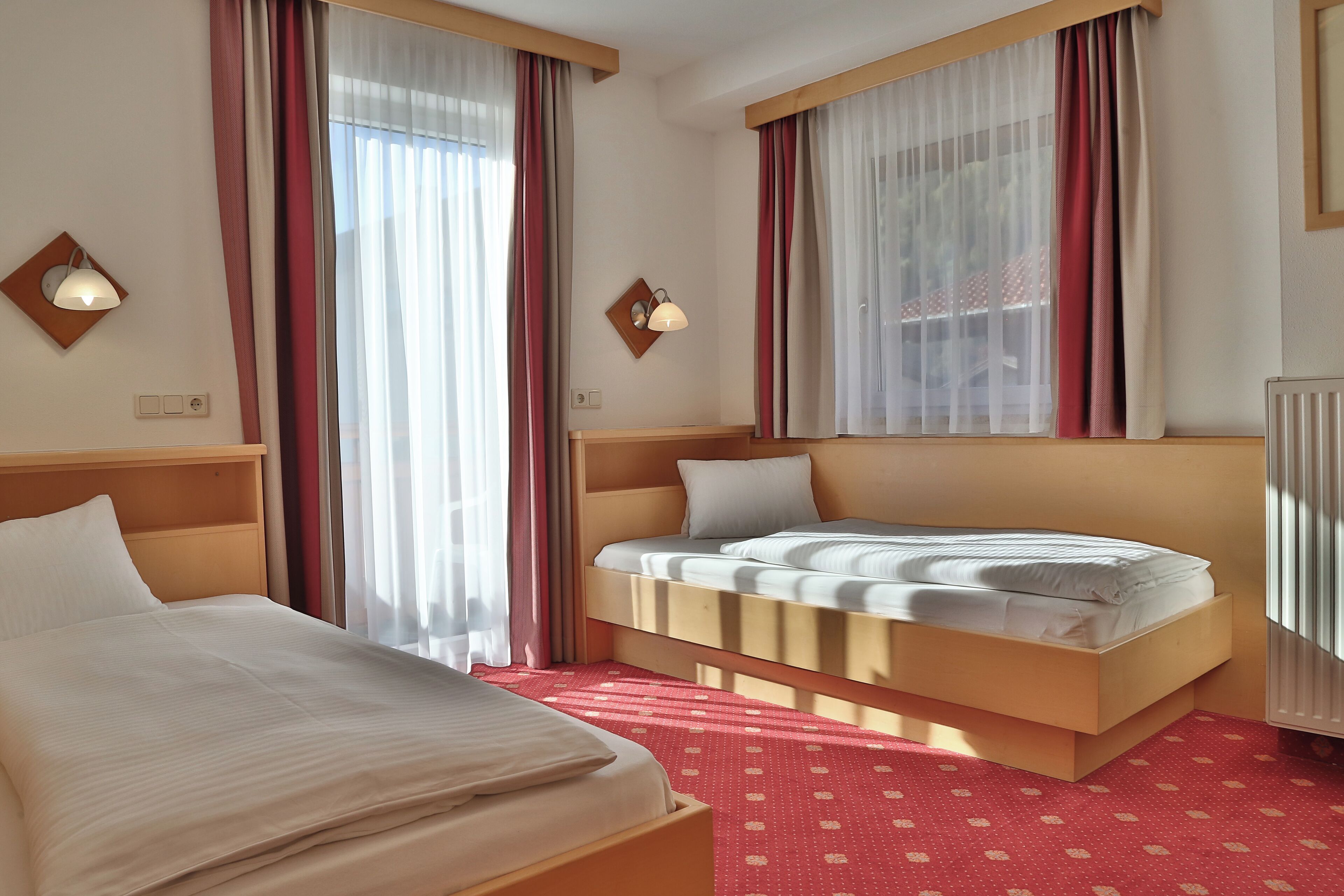 A hotel room with a bed, a nightstand, a wall-mounted lamp, and a window with curtains.